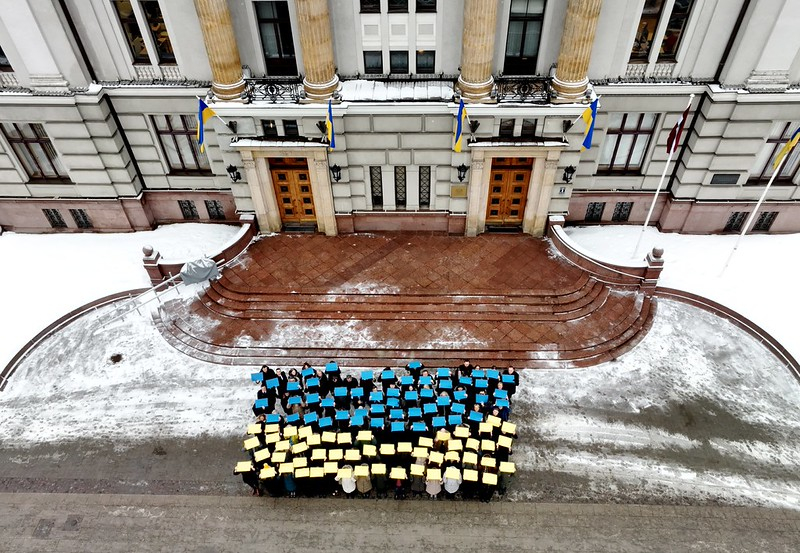 ĀM kolēģi un Ukrainas vēstniecības darbinieki turot rokās krāsainu papīru veido Ukrainas karoga formu