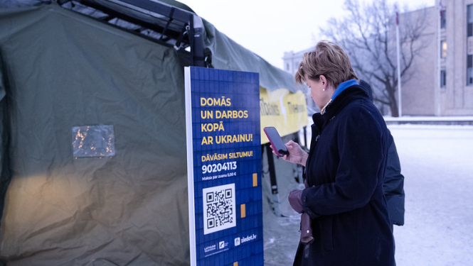 Baiba Braže pie Nesalaužamības punkta telts skanē "Ziedot.lv" akcijas "Siltums Ukrainai no Latvijas" QR kodu
