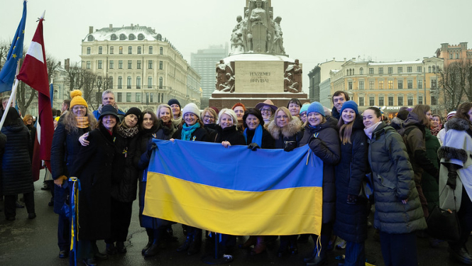 Diplomātiskā kora dalībnieki pie brīvības pieminekļa turot rokās Ukrainas karogu