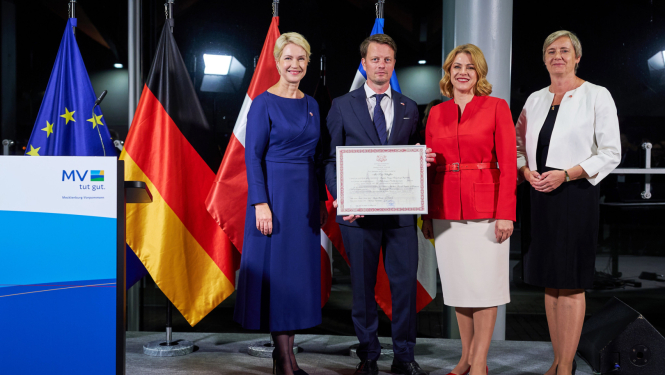 Mēklenburgas-Priekšpomerānijas Ministru prezidente Manuela Švēziga, jaunā Latvijas goda konsulāta Mēklenburgas-Priekšpomerānijas federālajā zemē vadītājs Toms Šeflers, Latvijas Ministru prezidente Evika Siliņa, Latvijas vēstniece Vācijā Alda Vanaga