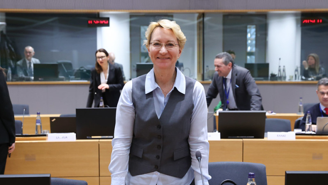 Dace Melbārde stāv pie galda sanāksmju zālē