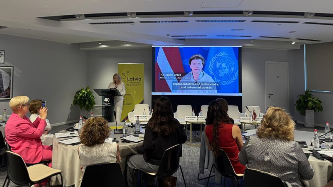 Dalībnieki pie apspriežu galda skatās Baibas Bražes uzrunu tiešsaistē