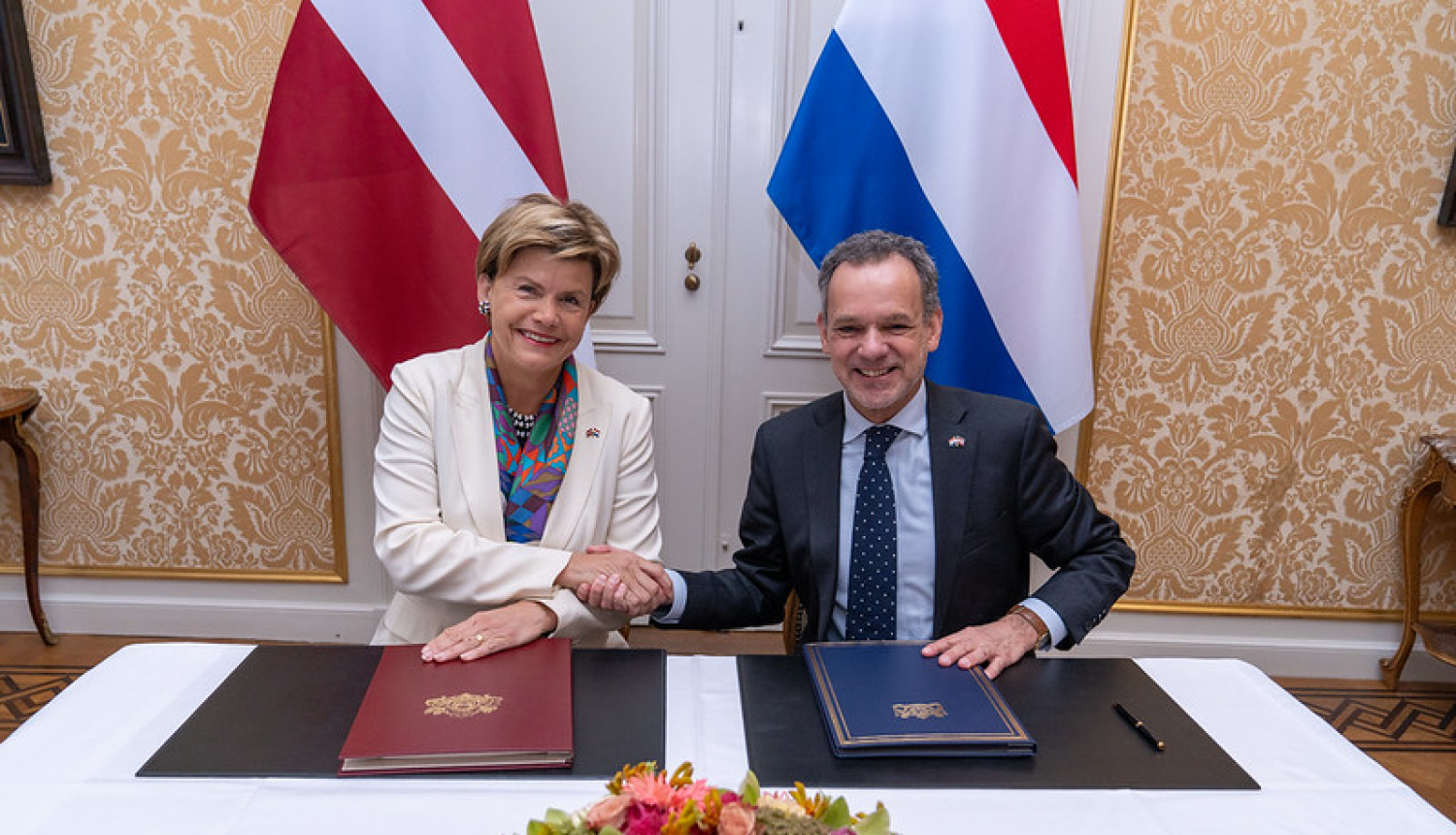 Baiba Braže un Caspar Veldkamp spiež rokas pēc līguma parakstīšanas