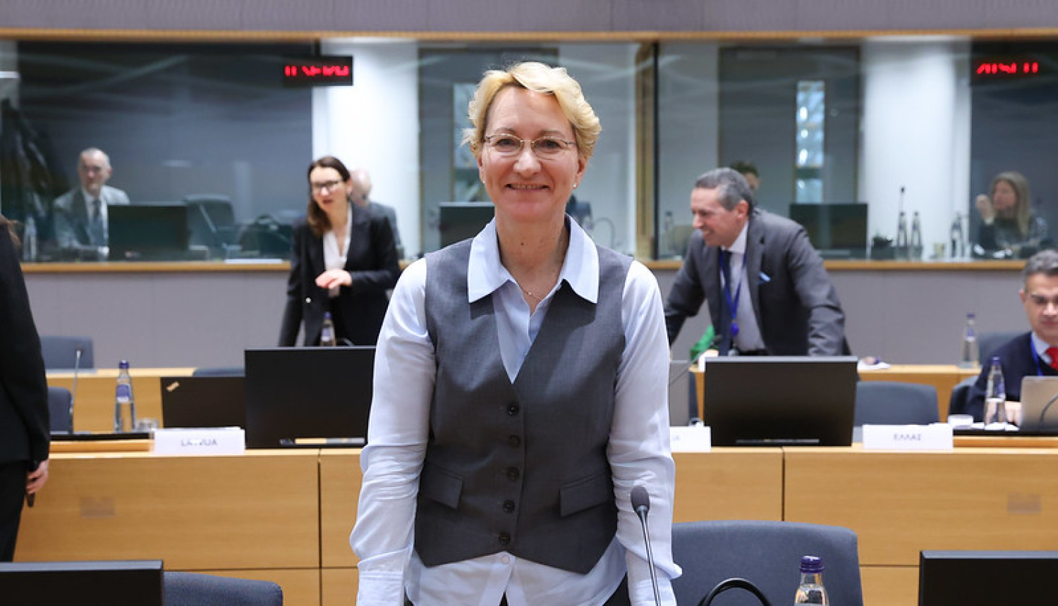 Dace Melbārde stāv pie galda sanāksmju zālē