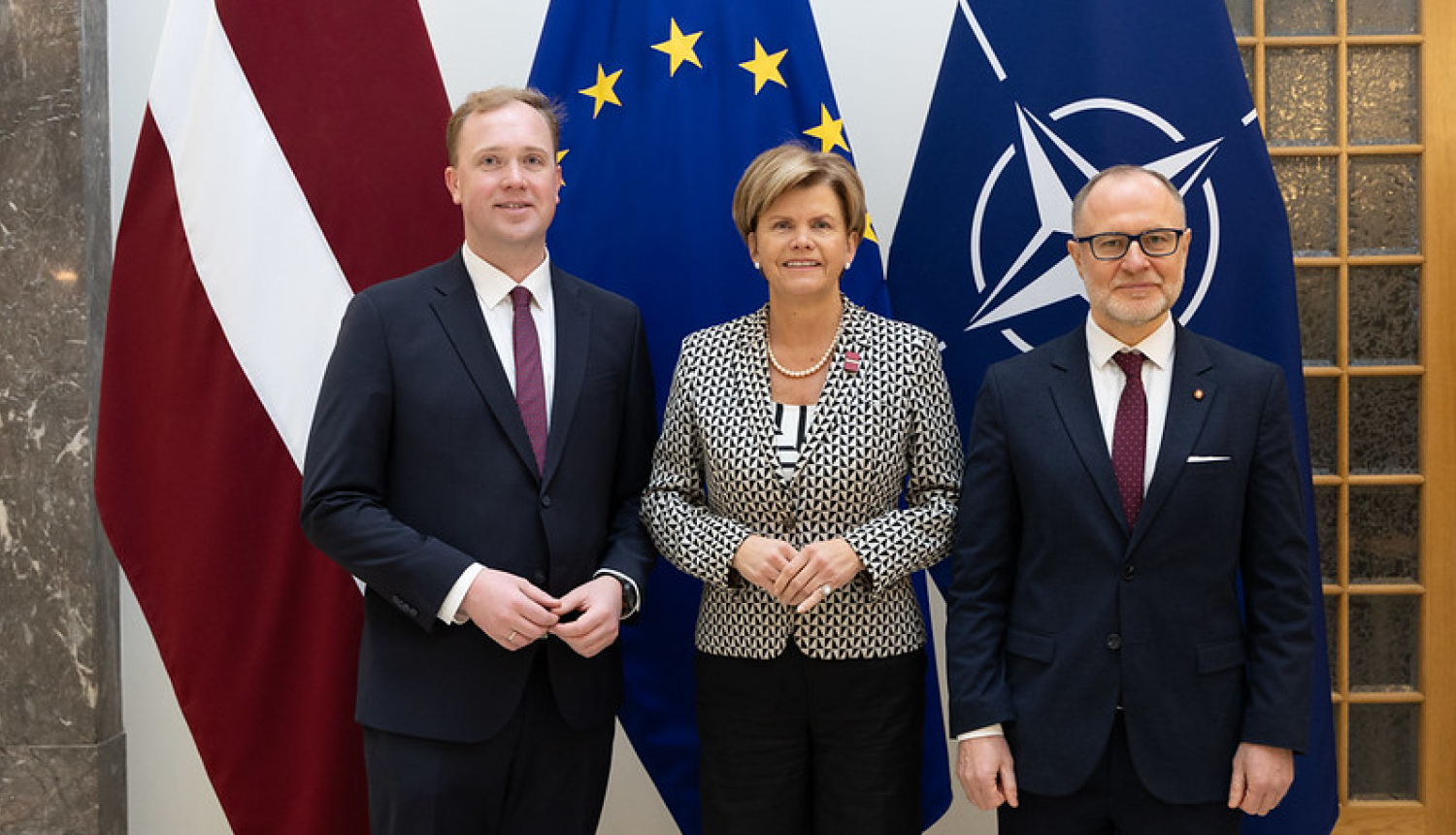 Ekonomikas ministrs Viktors Valainis, ārlietu ministre Baiba Braže un aizsardzības ministrs Andris Sprūds uz Latvijas, ES un NATO karogu fona