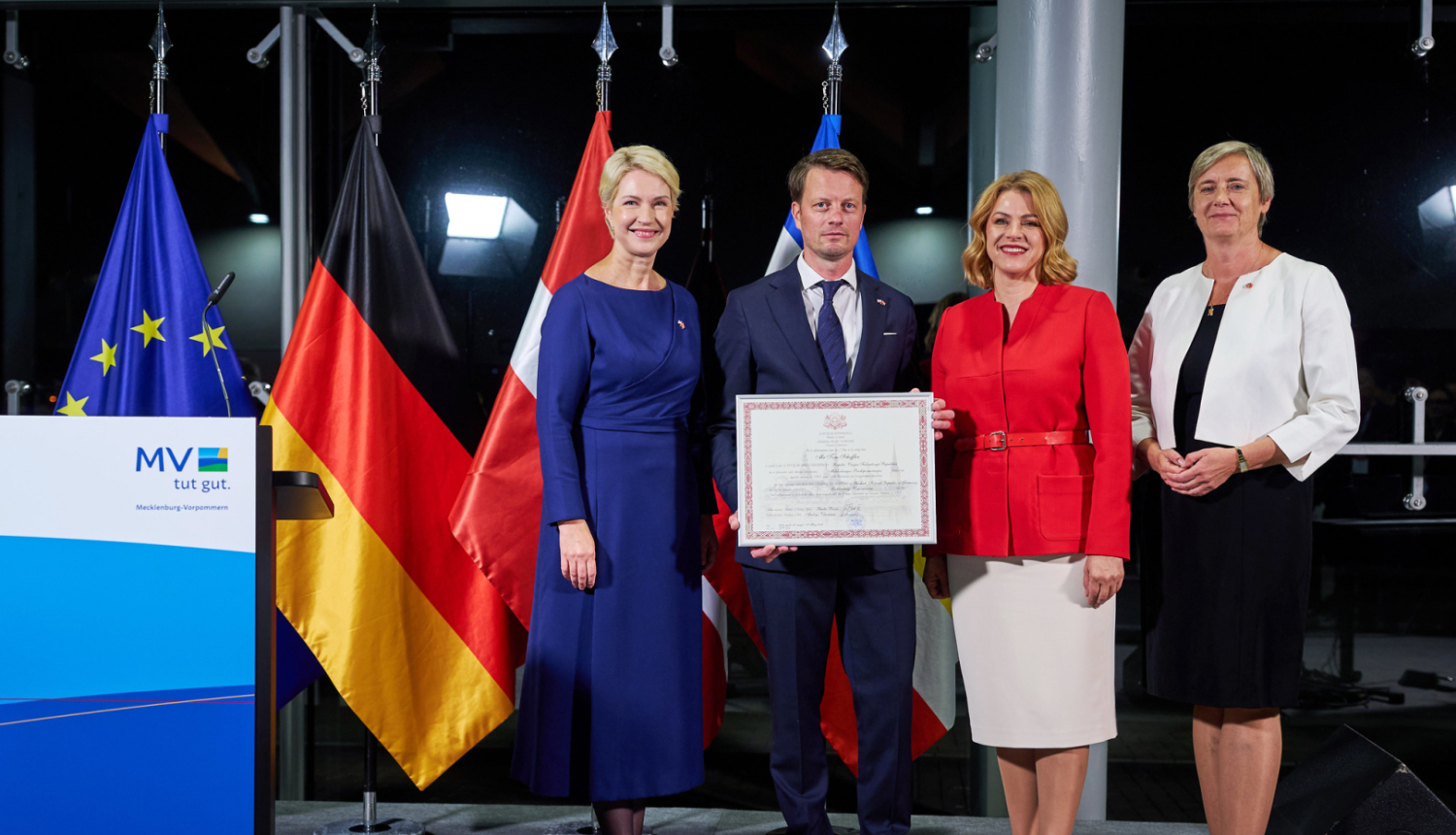 Mēklenburgas-Priekšpomerānijas Ministru prezidente Manuela Švēziga, jaunā Latvijas goda konsulāta Mēklenburgas-Priekšpomerānijas federālajā zemē vadītājs Toms Šeflers, Latvijas Ministru prezidente Evika Siliņa, Latvijas vēstniece Vācijā Alda Vanaga