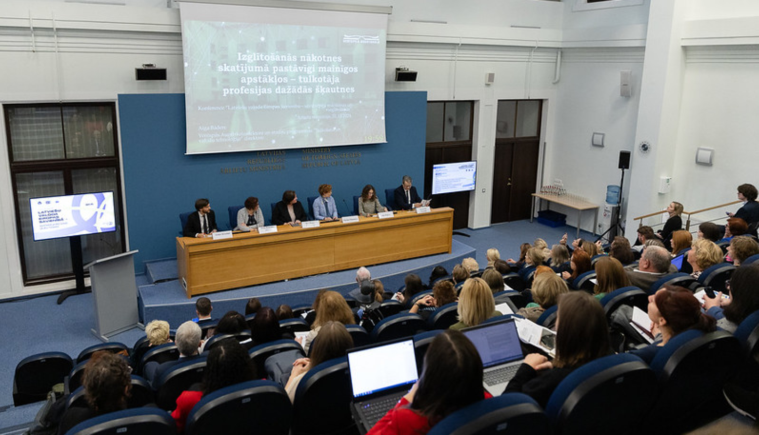 Pasākuma zāles kopskats ar runātājiem un apmeklētājiem