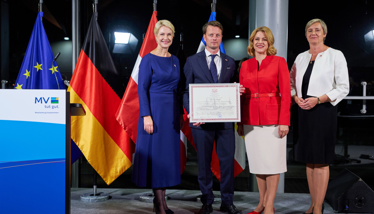 Mēklenburgas-Priekšpomerānijas Ministru prezidente Manuela Švēziga, jaunā Latvijas goda konsulāta Mēklenburgas-Priekšpomerānijas federālajā zemē vadītājs Toms Šeflers, Latvijas Ministru prezidente Evika Siliņa, Latvijas vēstniece Vācijā Alda Vanaga